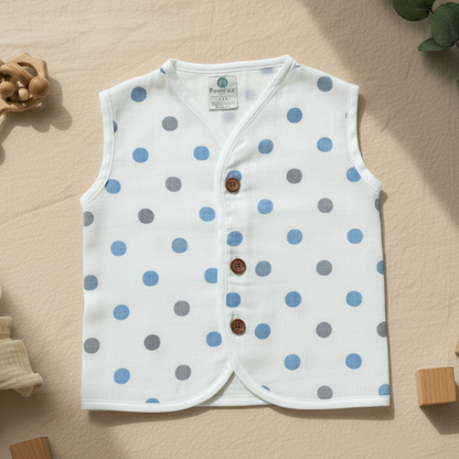 White children's vest with blue and gray polka dots on a beige surface with toys.