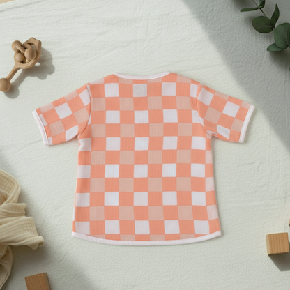 Checkered baby shirt on a light surface with toys and a plant